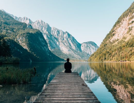 homme au bord d'un ponton avec vue sur un lac et montagne