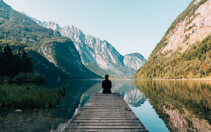 homme au bord d'un ponton avec vue sur un lac et montagne